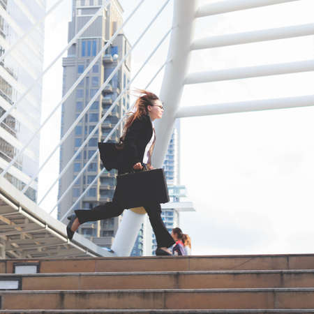 Business woman  holding bag and running rapidly to airport in formal suit. In rush hour at stairway in city. Business in the city concept.の写真素材