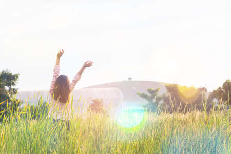 Young woman standing at relax pose or freedom pose or chill pose on the meadow during sunrise at morning.の写真素材