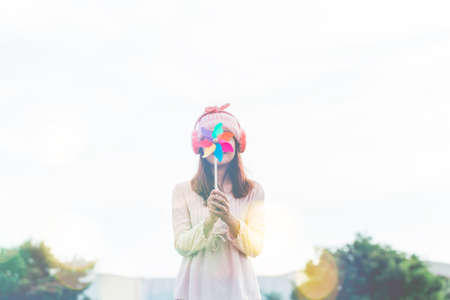 Silhouette of Beautiful girl holding wind toy or wind turbine or pinwheel and wool hat at meadow on winter season in morning.の写真素材