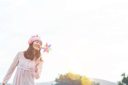 Silhouette of Beautiful girl holding wind toy or wind turbine or pinwheel and wool hat at meadow on winter season in morning.の写真素材