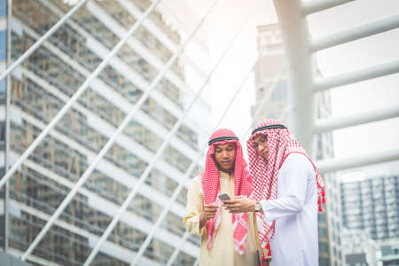 Two Arab or Muslim business man standing at front modern office discussing work with smart phone. Ethnic business people in urban concept.の写真素材