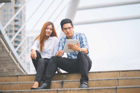 Young Businessman and businesswoman using digital tablet with colleagues in background at walkway at...