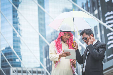 Arabic businessman looking tablet with his bodyguard on cityscape backgroundの写真素材
