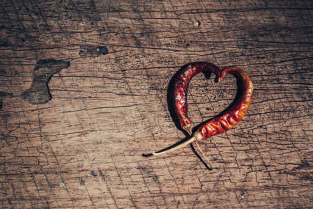 Two chili peppers forming a shape of heart on old wooden background. Love valentine concept.の写真素材
