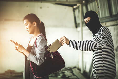 Thief stealing wallet from pocket women while her playing smart phone at side way. criminal and robbery for women concept.の写真素材