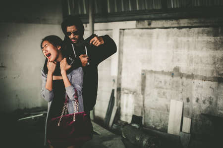 Man in hoodie robbing and threatening with gun to frightened young woman. criminal and robbery for woman concept.の写真素材