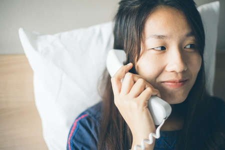Attractive young woman lying on bed and talking on old retro telephone in the  hotel roomの写真素材