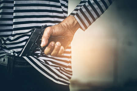 Robber pulls out a gun tucked in his jean. criminal and robbery concept.の写真素材