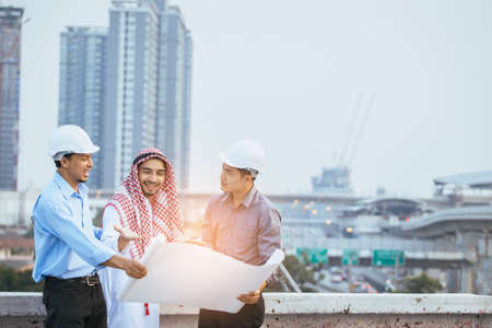 Muslim Business and Engineer working concept: two engineers and muslim businessmen discussing about plan of building site construction progression with layout paper at deck of their building.の写真素材