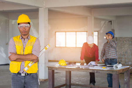 Portrait of confident Labor standing at front of engineer and foreman with safety helmet and level...