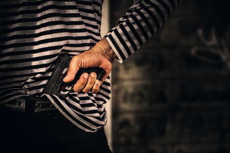 Robber pulls out a gun tucked in his jean. criminal and robbery concept.の写真素材