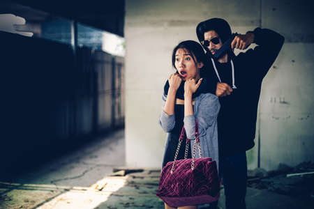 Man in hoodie robbing and threatening with gun to frightened young woman. criminal and robbery for woman concept.の写真素材