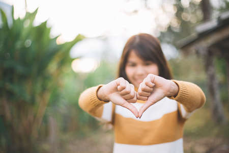 Heart shape made with hands of young women wearing a sweater in  green natural background. Love symbol concept.の写真素材