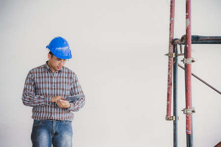 Portrait of confident foreman standing and holding tablet with safety helmet and scaffolding on old buildings in his job site.の写真素材