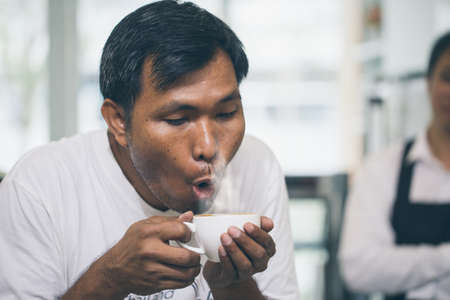 A man gestures surprise in his late art in the coffee cup he was holding. while Barista stand beside the bar.の写真素材