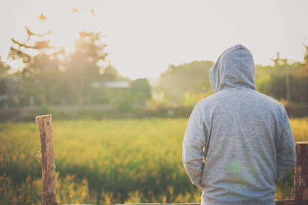 A man wearing a jacket with hood and standing with his back in a meadow with sunlight in the morning. Winter season concept.の写真素材