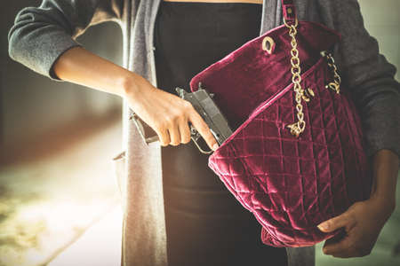 Woman pulls a gun from her swanky purse. Conceal carry weapon for protection themselves concept. Selective focus to gun.の写真素材