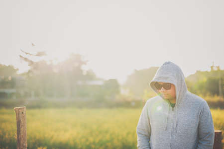 A man wearing a jacket with hood and standing  in a meadow with sunlight in the morning. Winter season concept.の写真素材