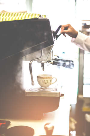 Barista releasing stream by cofee machine with cup for prepares espresso coffee in his coffee shop.の写真素材