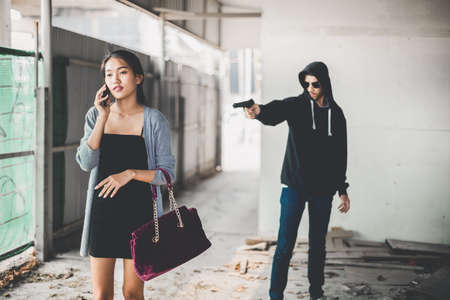 Man in hoodie robbing and threatening with gun to frightened young woman. criminal and robbery for woman concept.の写真素材