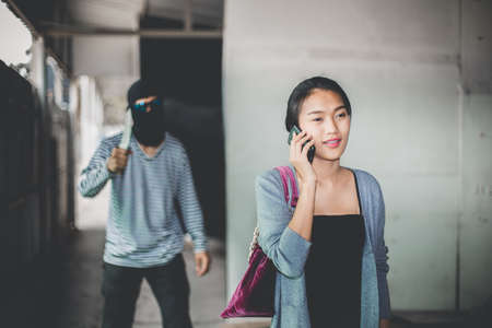 Man in hoodie robbing and threatening with gun to frightened young woman. criminal and robbery for woman concept.の写真素材