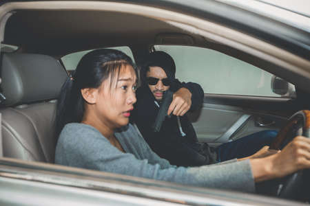 A robber dressed in black pointing a gun at a women driver in a car. Car theft of a womanの写真素材