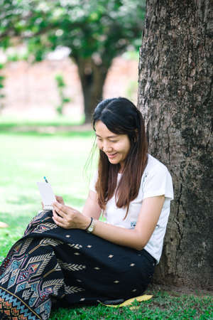 young woman sitting under a tree and writing her diary. women with natural conception.の写真素材