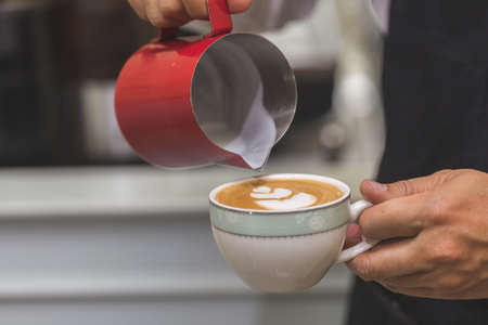 Hand of barista pouring milk make coffee latte art with white cup in cofee shop. Heart coffee latte art.の写真素材