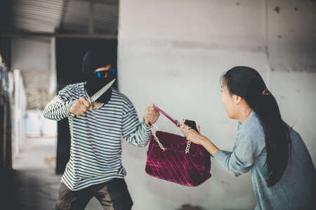 Man in hoodie robbing and threatening with gun to frightened young woman. criminal and robbery for woman concept.の写真素材