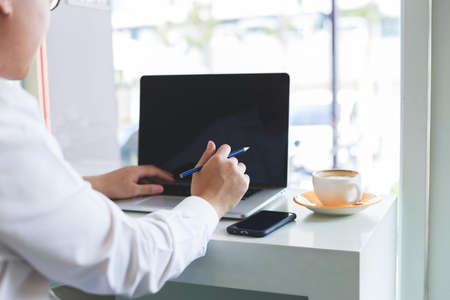 Young asian businessman sitting in cafe with cup of coffee and working his job by laptop connecting wifi internet. Business in cafe concept.の写真素材