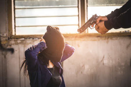 A terrorist man holding gun kidnapping young women for a hostage in abandoned building. Rape, terrorism, crime, violence, robbery and killer of women conception.の写真素材