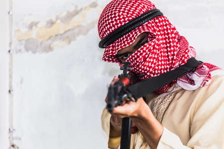 Muslim Robber holding a gun at abandoned building. Low key photo and selective focus. criminality concept.の写真素材