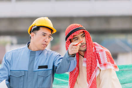 Arabian businessman or Arabian engineer and Laborer working and discussion of blueprint on construction plans front of building in his work site. Teamwork conceptの写真素材
