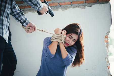 Man in hoodie robbing and threatening with gun to frightened young woman. criminal and robbery for woman concept.の写真素材