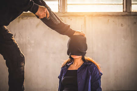 A terrorist man holding gun kidnapping young women for a hostage in abandoned building. Rape, terrorism, crime, violence, robbery and killer of women conception.の写真素材