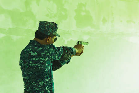 The soldier in the performance of tasks in camouflage holding a pistol with the hammer cocked takes aim for shot. War zone. Secret mission concept. Green tone effect.の写真素材