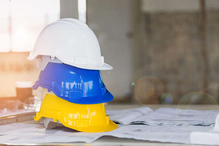 The white, blue and yellow safety helmet stacking on table with the blueprint and measuring tools  at construction site for Engineer, foreman and worker. Safety first concept.の写真素材