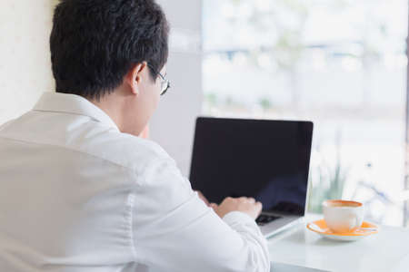 Young asian businessman sitting in cafe with cup of coffee and working his job by laptop connecting wifi internet. Business in cafe concept.の写真素材