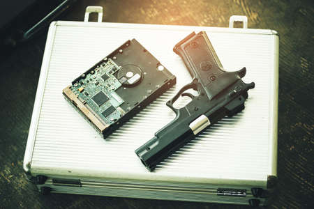 Computer hard drive and short gun put on a briefcase. Terrorist and hacker concept.