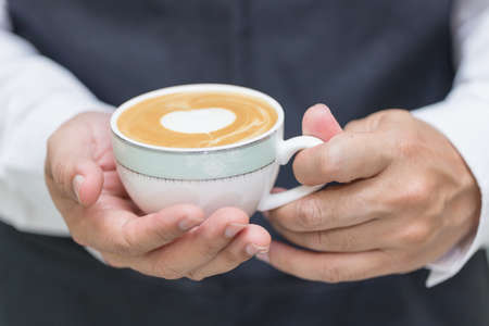 Barista holding cup of heart latte art coffee in cafe.の写真素材