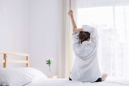 Happy woman stretching on bed after waking up in the early morning at window side. Have a good day.の写真素材