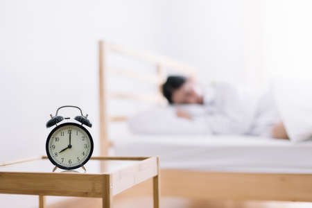 Close up alarm clock. Happy woman being drowsy on bed after waking up in the early morning at window side. Have a good day.の写真素材