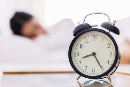Close up alarm clock. Happy woman being drowsy on bed after waking up in the early morning at window...