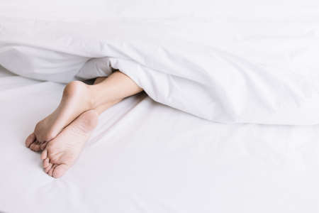 Woman Feet on a white bed against white quilt in early morning.の写真素材