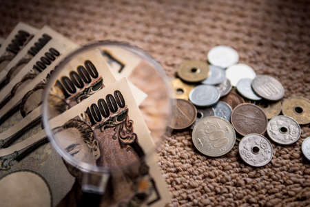 Japanese Yen Banknotes and Japanese Yen coin shot stack layers on floor with magnifying glass for...