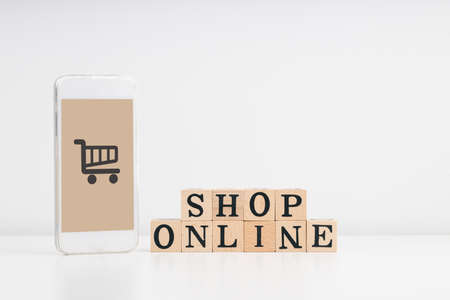 Shopping online, Shop from home, and home delivery concept. SHOP ONLINE wording on a stack of wooden blocks and smartphone mockup with cart icon. white background.home deliveryの写真素材