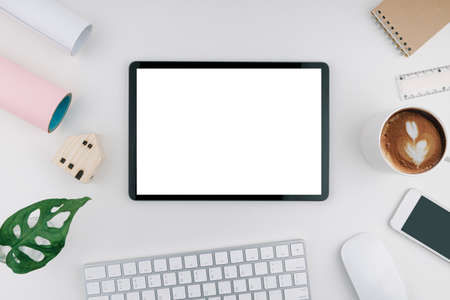 Tablet with blank and white screen on desk including a wooden mini house. keyboard, mouse,...