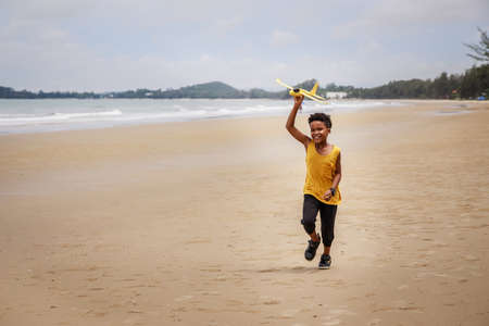 Happy colored boy and African American boy playing yellow toy airplane and running by wearing yellow sweater. Having fun on beach after unlock down city from COVID19. concept of dreams and travelsの写真素材