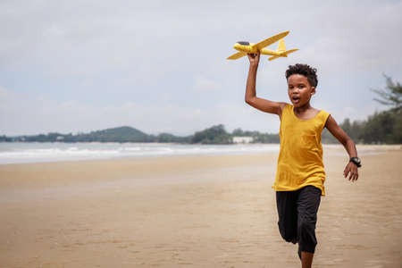 Happy colored boy and African American boy playing yellow toy airplane and running by wearing yellow...