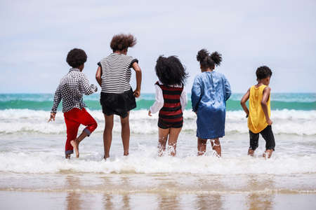 African American, Kids group in swimwear enjoying running to play the waves on beach. Ethnically diverse concept. Having fun after unlocking down from COVID 19. Summer holidays on beach with friendsの写真素材